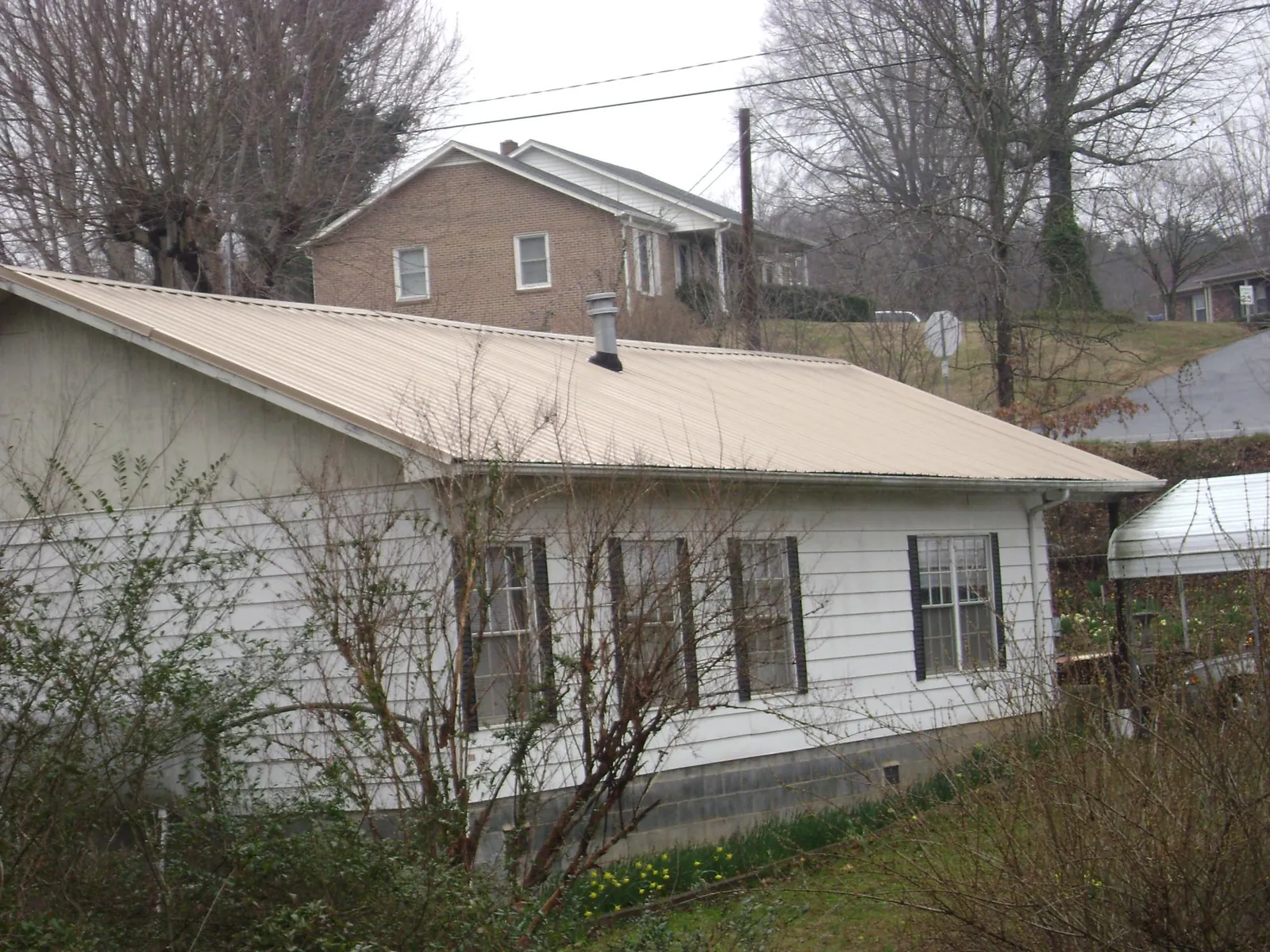 Tan metal roof on a white sided house set into a hillside — Commercial Roofing by Roofing Brothers in Leesburg