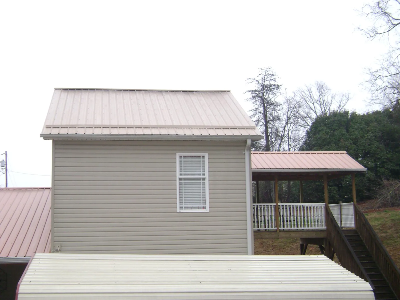 Tan metal roofs on a two story addition and attached porch, from a Roof Replacement job in Leesburg